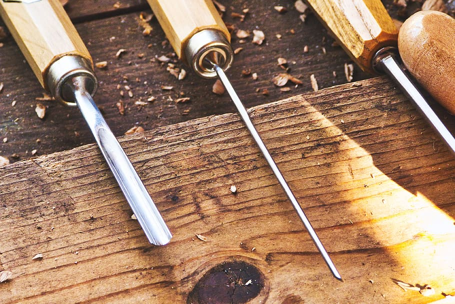 Set of wood carving tools on a wooden table. This image can be used to help people identify hand-carved furniture. Hand-carved furniture is made by hand using traditional tools and techniques. It is often made from natural materials, such as wood, and can have unique and intricate details. To tell if furniture is hand-carved, look for signs of unevenness or imperfections, as well as the use of natural materials. Vintage and antique furniture are often hand-carved, and can be a valuable investment.